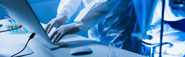 Abgeschnittene Ansicht eines Wissenschaftlers in Latexhandschuhen, der auf der Computertastatur im Labor tippt, Banner — Stockfoto