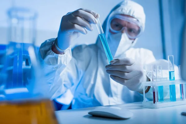 Cientista desfocado em terno hazmat segurando tubo de ensaio em laboratório químico — Fotografia de Stock