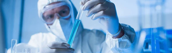 Bioengineer in goggles and medical mask holding test tube with liquid, banner — Stock Photo