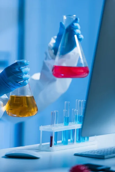 Vista recortada de los científicos sosteniendo frasco con líquido colorido en el laboratorio - foto de stock