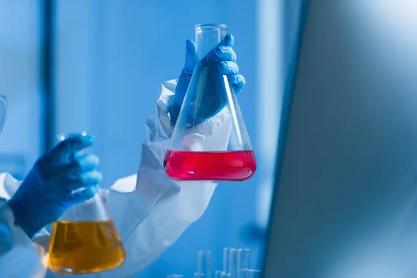 Frascos com líquido colorido nas mãos de cientista cultivado em laboratório — Fotografia de Stock