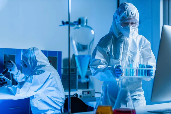 Биоинженер держит пробирки, пока коллега работает над фоном — стоковое фото