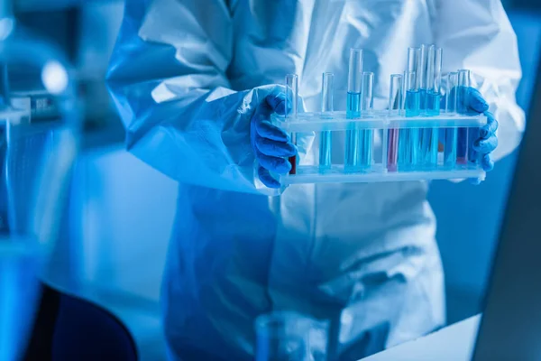 Partial view of bioengineer in hazmat suit holding test tubes in lab — Stock Photo