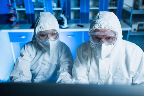 Cientistas em fatos de proteção contra riscos, óculos de proteção e máscaras médicas que trabalham em laboratório — Fotografia de Stock