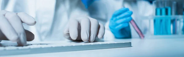 Teilansicht des Wissenschaftlers in Latexhandschuhen beim Tippen auf Computertastatur, Banner — Stockfoto