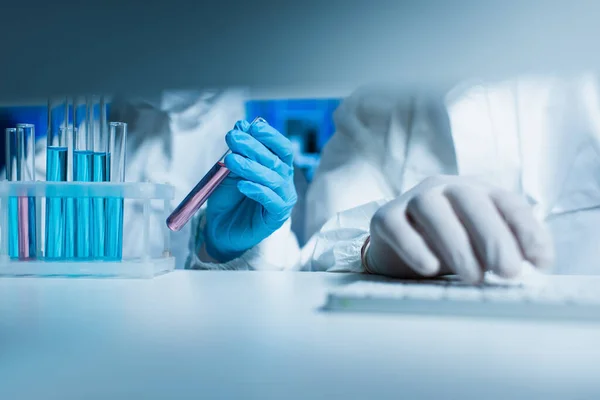 Cropped view of scientist holding test tube near colleague typing on computer keyboard — Stock Photo