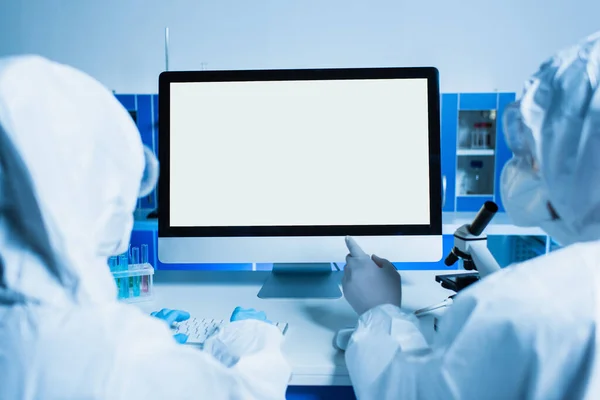 Back view of scientist pointing at monitor with white screen near colleague in lab — Stock Photo