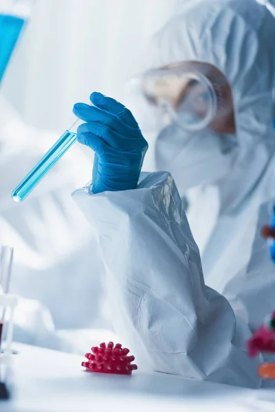 Blurred virologist holding test tube near model of coronavirus bacteria — Stock Photo