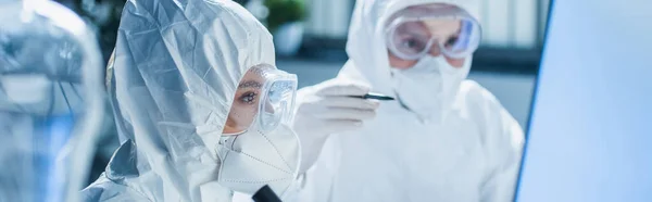 Bioingénieur en équipement de protection individuelle près d'un collègue pointant sur fond flou, bannière — Photo de stock