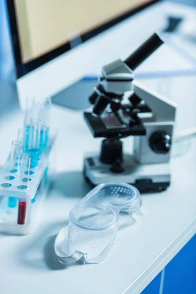 Goggles near blurred test tubes and microscope in laboratory — Stock Photo