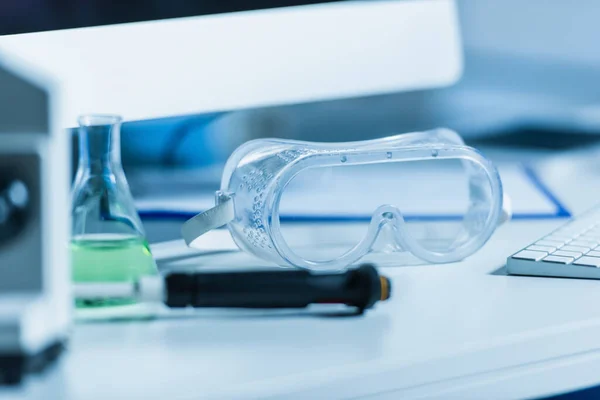 Selective focus of goggles on desk in bio laboratory on blurred foreground — Stock Photo