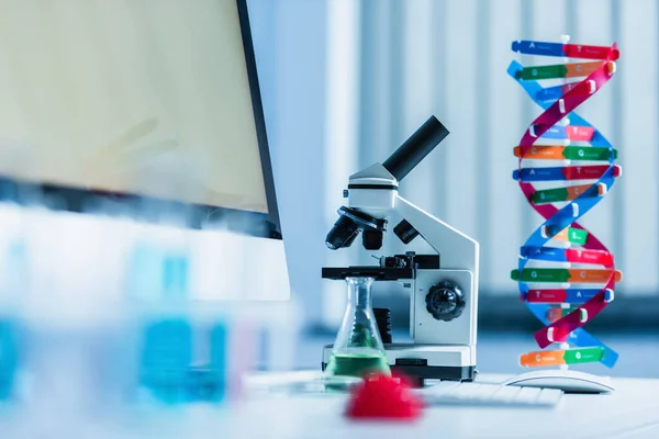 Modelo de microscópio e dna perto do monitor com tela cinza em primeiro plano desfocado — Fotografia de Stock