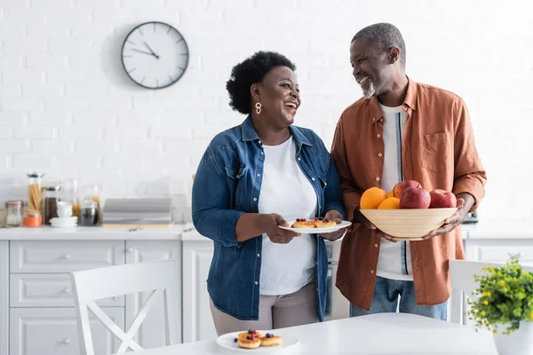 Glücklicher älterer afrikanisch-amerikanischer Mann hält Schale mit Früchten neben lächelnder Frau — Stockfoto