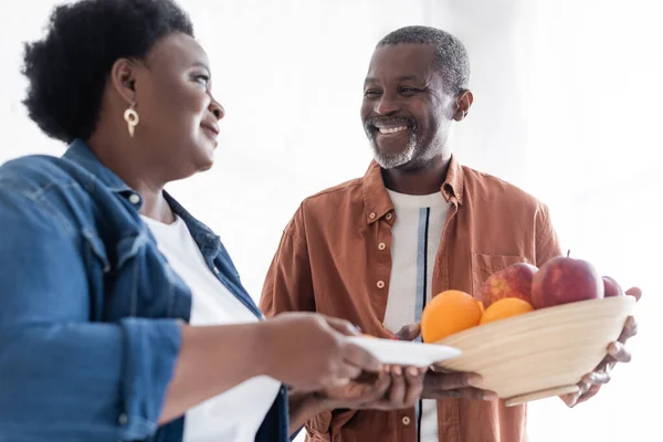 Felice uomo africano americano anziano che tiene ciotola con frutta fresca vicino moglie sorridente — Foto stock