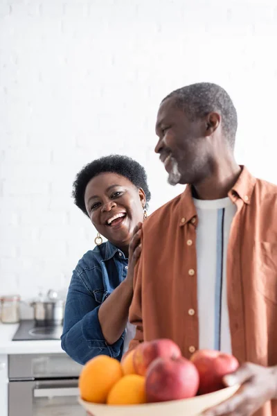 Anziano uomo africano americano che tiene ciotola con frutti sfocati vicino alla moglie sorridente — Foto stock