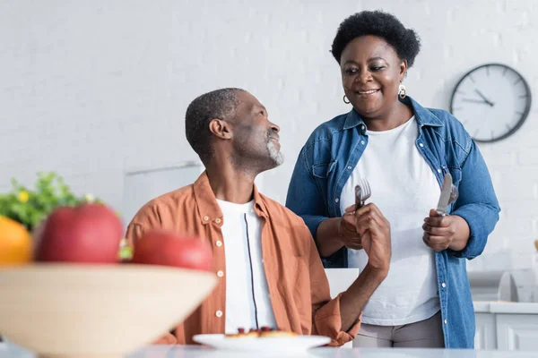 Happy and senior african american woman holding cutlery near smiling husband during breakfast — Stock Photo