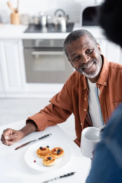 Glücklich afrikanisch-amerikanischer Mann schaut Frau beim Frühstück an, die Tasse hält — Stockfoto