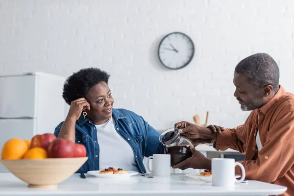 Älterer afrikanisch-amerikanischer Mann schenkt seiner glücklichen Frau während des Frühstücks Kaffee ein — Stockfoto