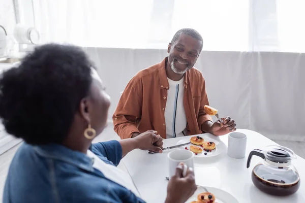 Alegre e sênior casal afro-americano de mãos dadas enquanto toma café da manhã — Fotografia de Stock