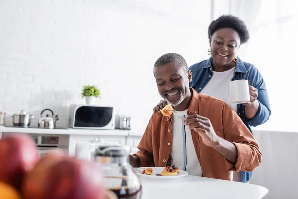 Homem americano africano sênior comendo panquecas perto da esposa feliz — Fotografia de Stock