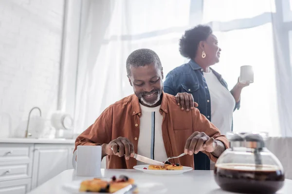 Sênior africano americano homem tomando café da manhã perto feliz esposa — Fotografia de Stock