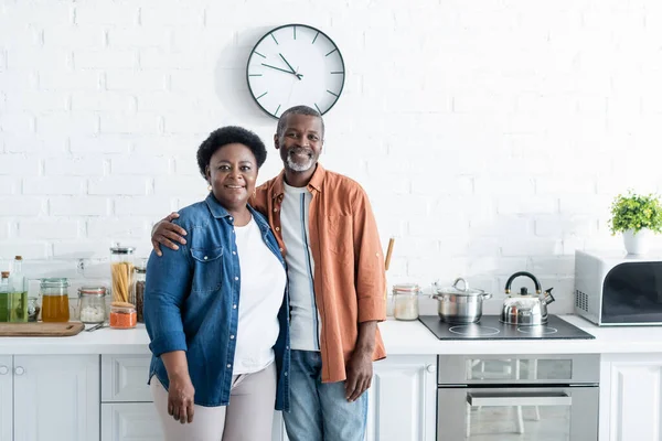 Happy senior african american couple looking at camera in kitchen — Stock Photo
