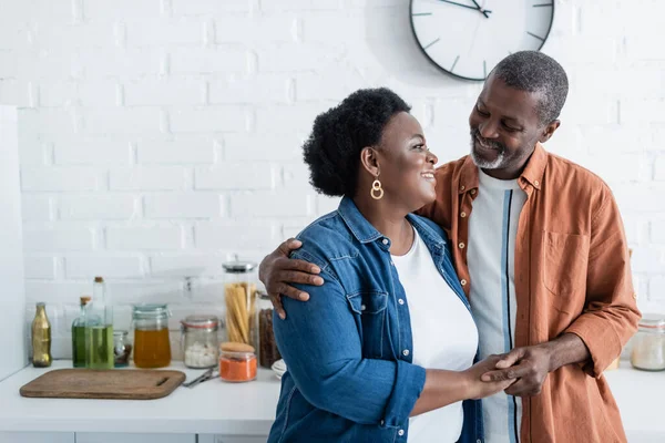 Feliz sénior afroamericano hombre mirando esposa en cocina - foto de stock