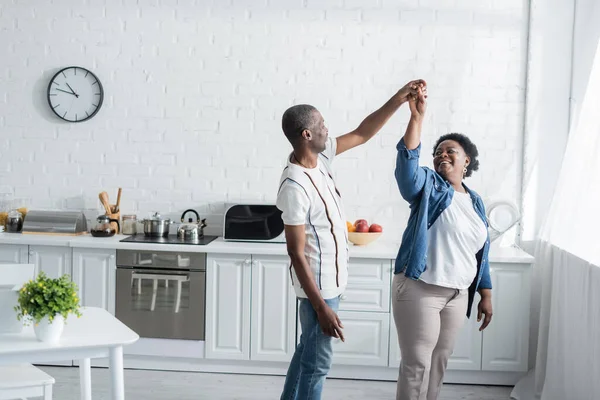 Retraité couple afro-américain souriant tout en dansant dans la cuisine — Photo de stock