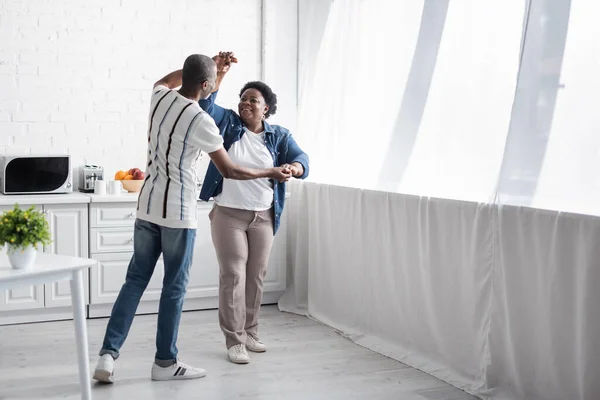 Full length of cheerful senior african american couple dancing in kitchen — Stock Photo