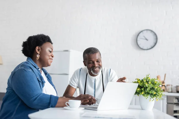 Alegre pareja afroamericana senior mirando portátil durante la videollamada - foto de stock