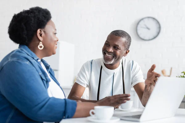 Alegre senior africano americano pareja mirando el uno al otro cerca de portátil - foto de stock