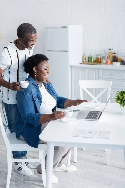 Позитивна і старша афроамериканська пара дивиться на ноутбук під час відеочату — стокове фото