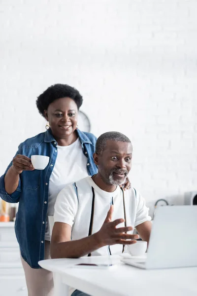 Shocked african american man gesturing near wife while looking at laptop — Stock Photo