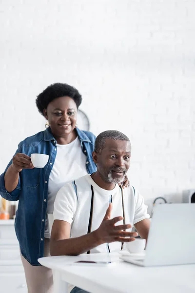 Choqué homme afro-américain geste près de la femme tout en regardant ordinateur portable — Photo de stock