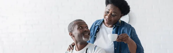 Bärtiger afrikanisch-amerikanischer Mann schaut Frau mit Tasse an, Banner — Stockfoto