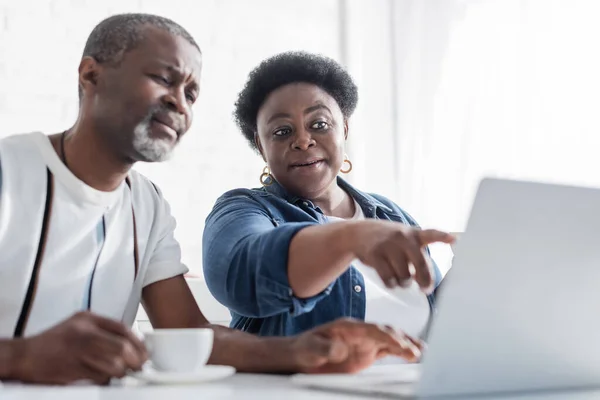Afrikanisch-amerikanische Rentnerin zeigt in der Nähe ihres Mannes auf Laptop — Stockfoto