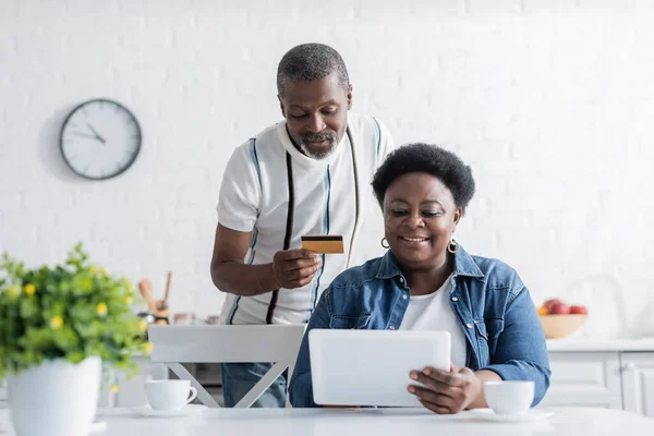Senior african american man holding credit card while online shopping with happy wife — Stock Photo