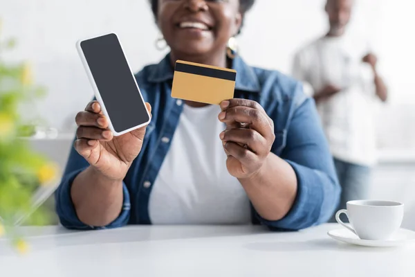 Vista ritagliata di felice anziana donna africana americana in possesso di carta di credito e smartphone con schermo bianco — Foto stock