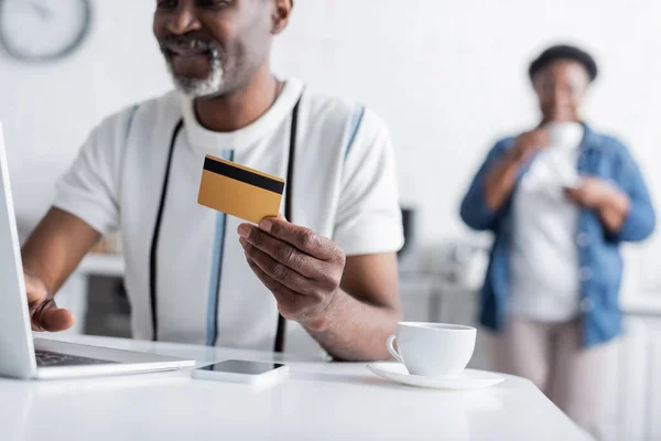 Vista cortada do homem americano africano sênior feliz que prende o cartão de crédito perto do portátil — Fotografia de Stock
