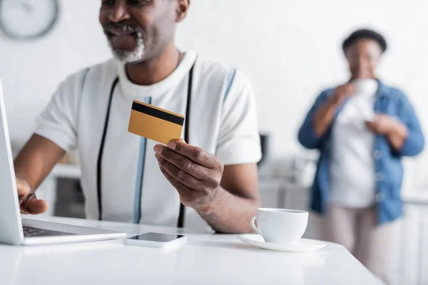Cropped view of happy senior african american man holding credit card near laptop — Stock Photo