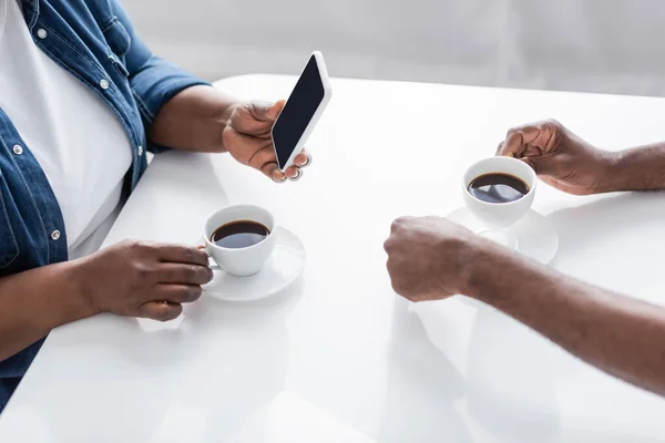 Cropped view of senior african american woman holding smartphone near husband and cups on table — Stock Photo