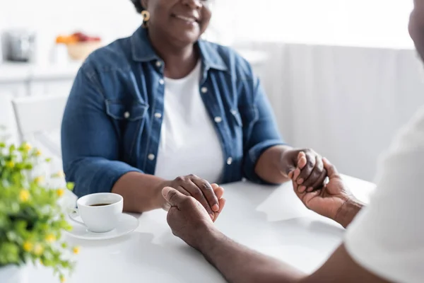 Vista recortada de la feliz pareja afroamericana de alto nivel tomados de la mano cerca de la taza de café - foto de stock