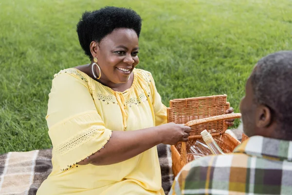 Feliz africano americano mujer sonriendo cerca marido durante picnic - foto de stock