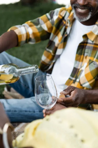Cropped view of senior african american man smiling and pouring wine into glass — Stock Photo