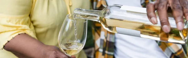 Cropped view of senior african american man pouring wine into glass near wife, banner — Stock Photo