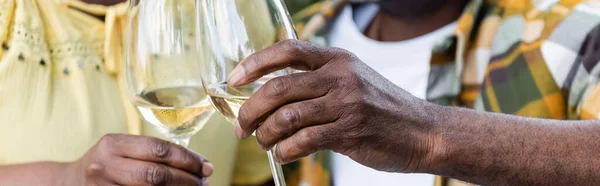 Vista recortada de la pareja afroamericana senior tintineo vasos de vino, pancarta - foto de stock