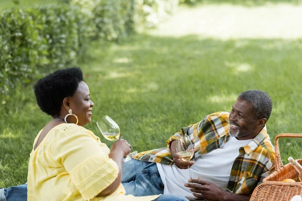Cheerful and senior african american couple drinking wine during picnic — Stock Photo