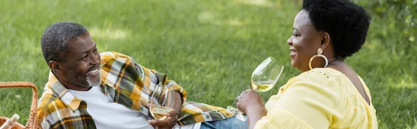 Cheerful and senior african american couple drinking wine during picnic, banner — Stock Photo