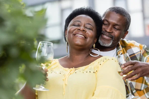 Joyful and senior african american couple holding glasses of wine — Stock Photo