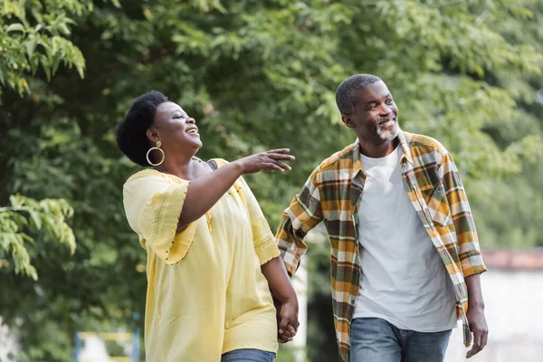 Feliz adulto mayor afroamericano pareja cogido de la mano y caminando en parque - foto de stock